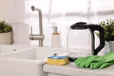 Photo of Cleaning electric kettle. Rubber gloves and sponge with foam on countertop in kitchen