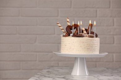 Photo of Delicious cake decorated with sweets and burning candles on white marble table, space for text