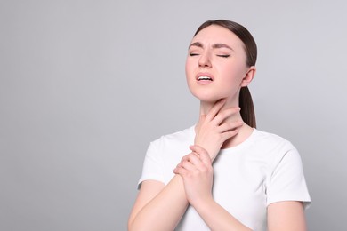 Young woman with sore throat on light grey background. Space for text