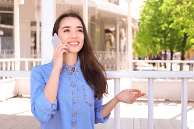 Photo of Young woman talking by phone outdoors on sunny day