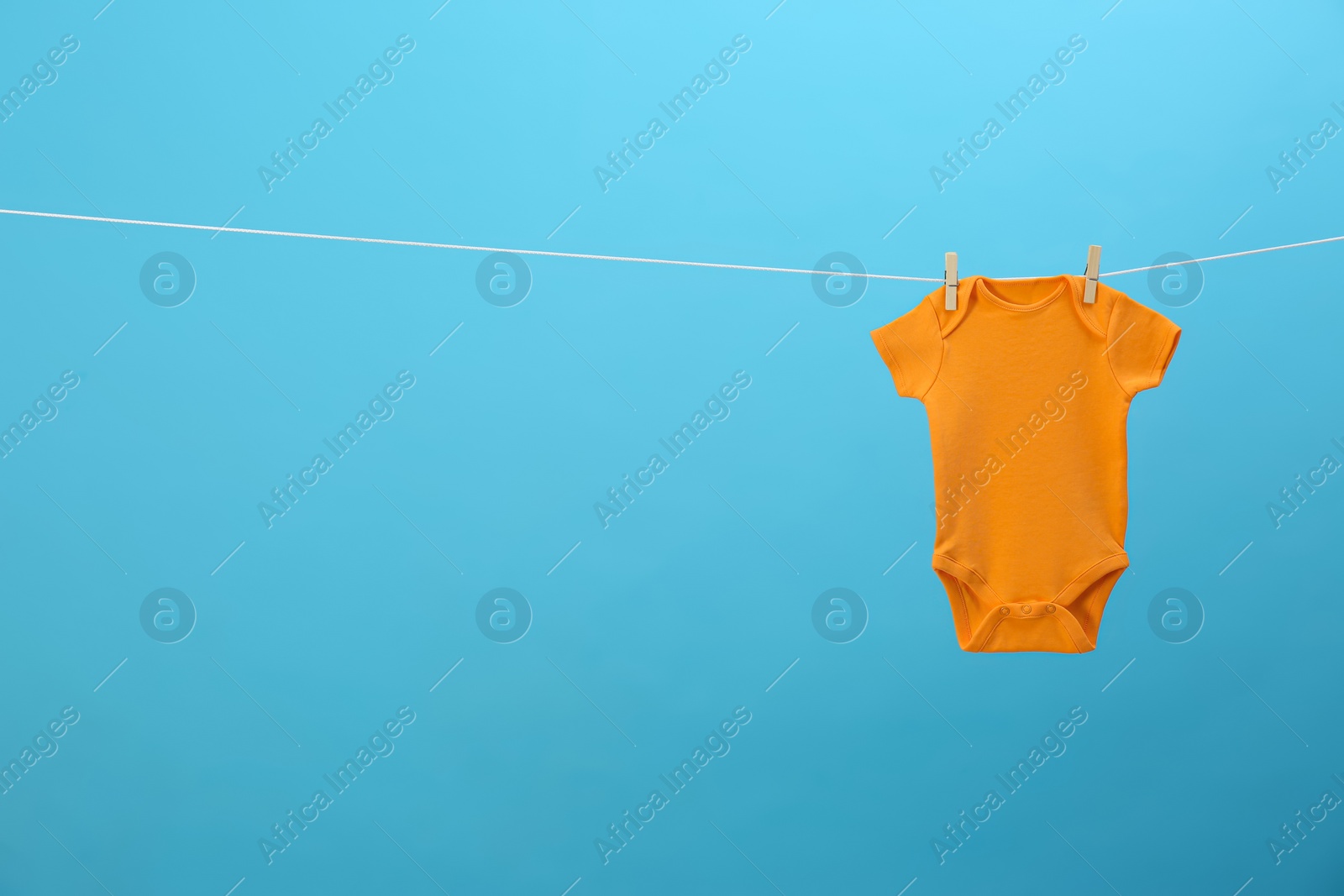 Photo of Baby onesie hanging on clothes line against blue background, space for text. Laundry day