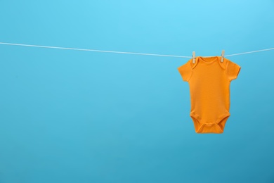 Baby onesie hanging on clothes line against blue background, space for text. Laundry day