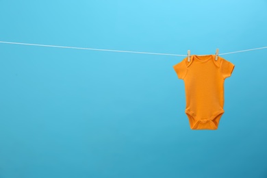 Photo of Baby onesie hanging on clothes line against blue background, space for text. Laundry day