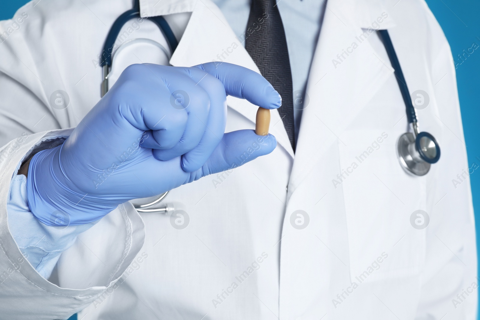 Photo of Doctor holding suppository for hemorrhoid treatment on blue background, closeup