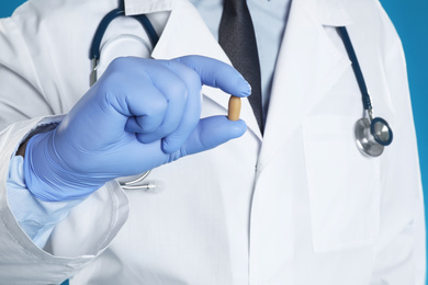 Doctor holding suppository for hemorrhoid treatment on blue background, closeup