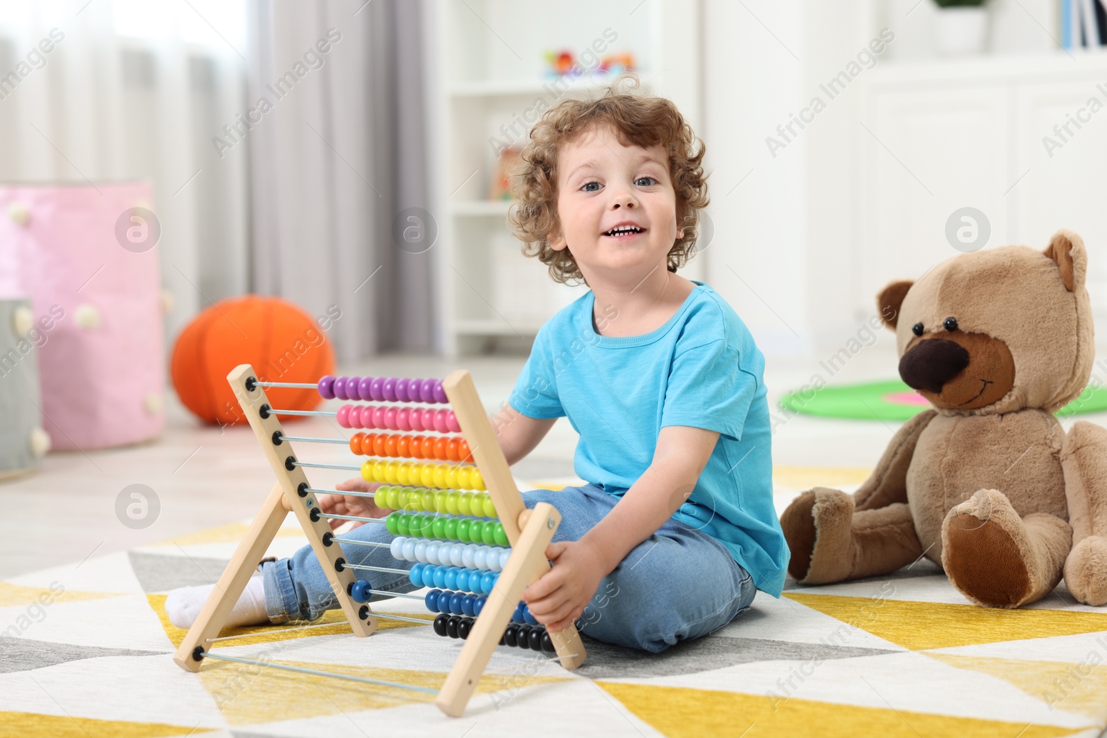 Photo of Cute little boy playing with wooden abacus on floor in kindergarten