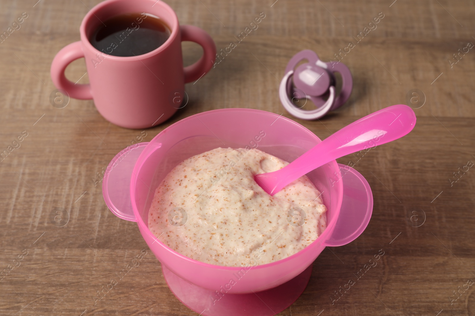 Photo of Baby food. Puree in bowl, drink and soother on wooden table