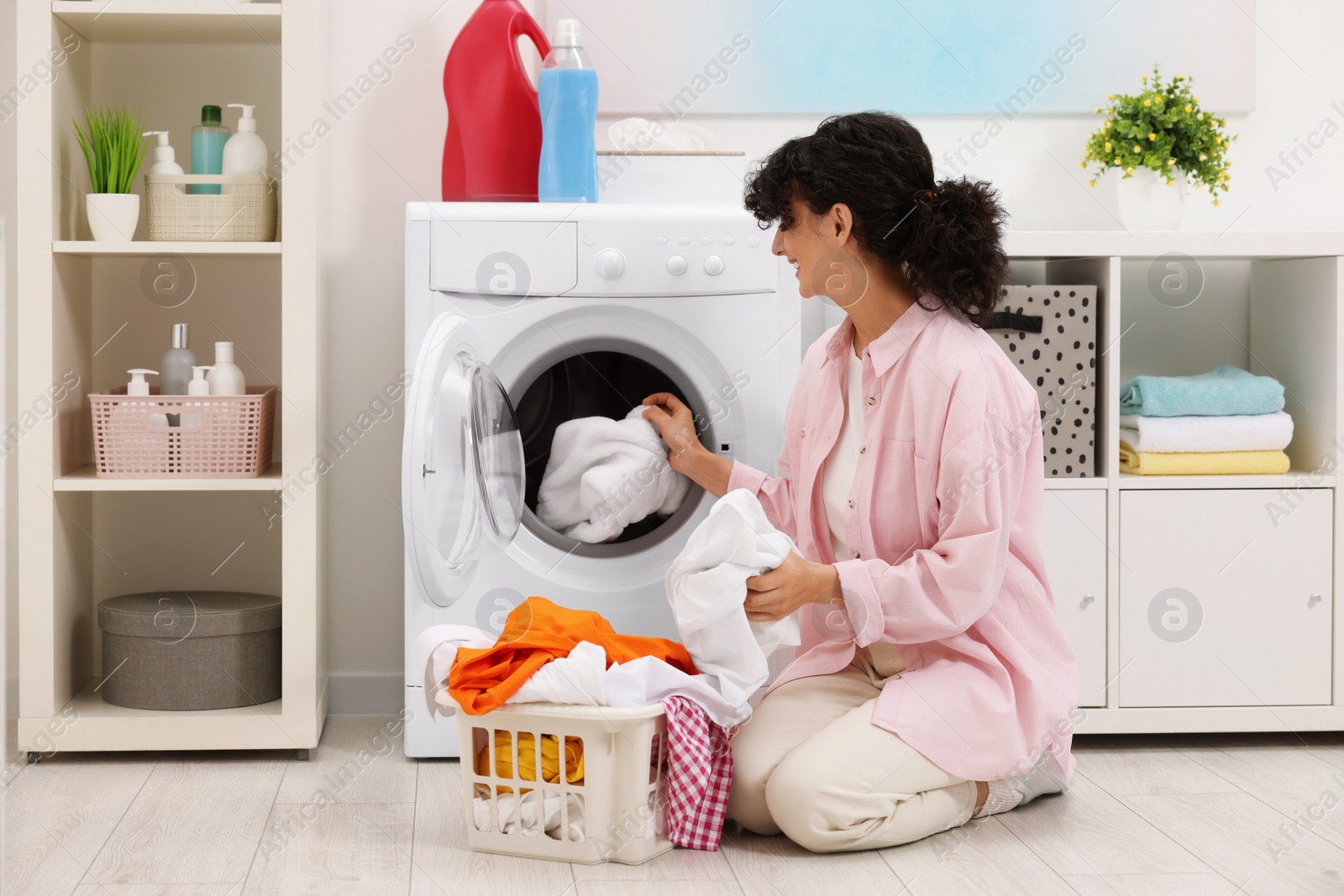 Photo of Happy woman putting laundry into washing machine indoors