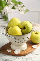 Colander with fresh apples and flower petals on white marble table