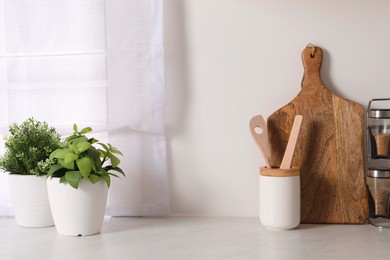 Photo of Artificial potted herbs and utensils on white marble table in kitchen. Home decor