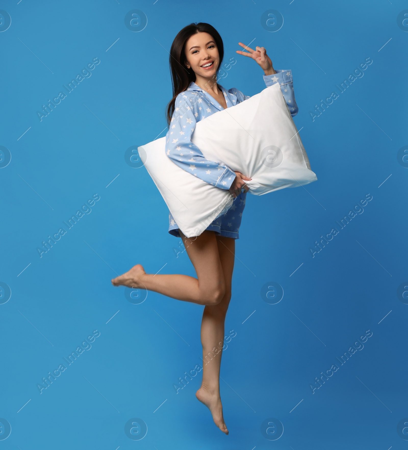 Photo of Beautiful Asian woman with pillow jumping on blue background. Bedtime