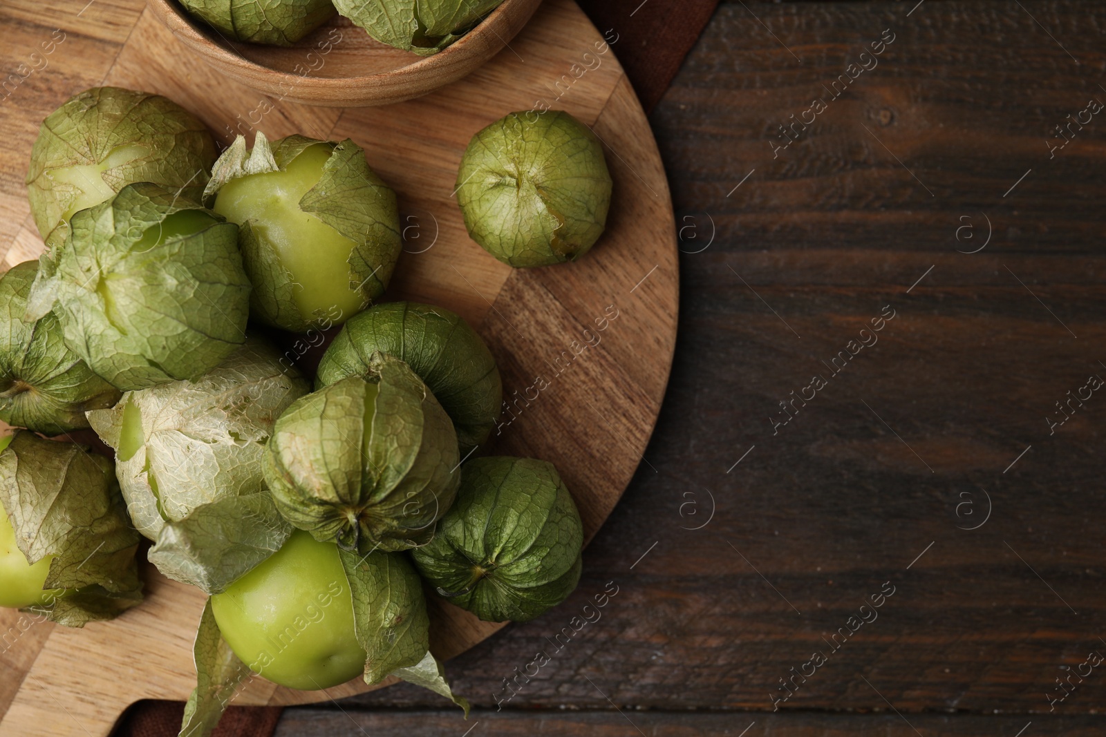 Photo of Fresh green tomatillos with husk in bowl on wooden table, top view. Space for text