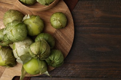 Photo of Fresh green tomatillos with husk in bowl on wooden table, top view. Space for text