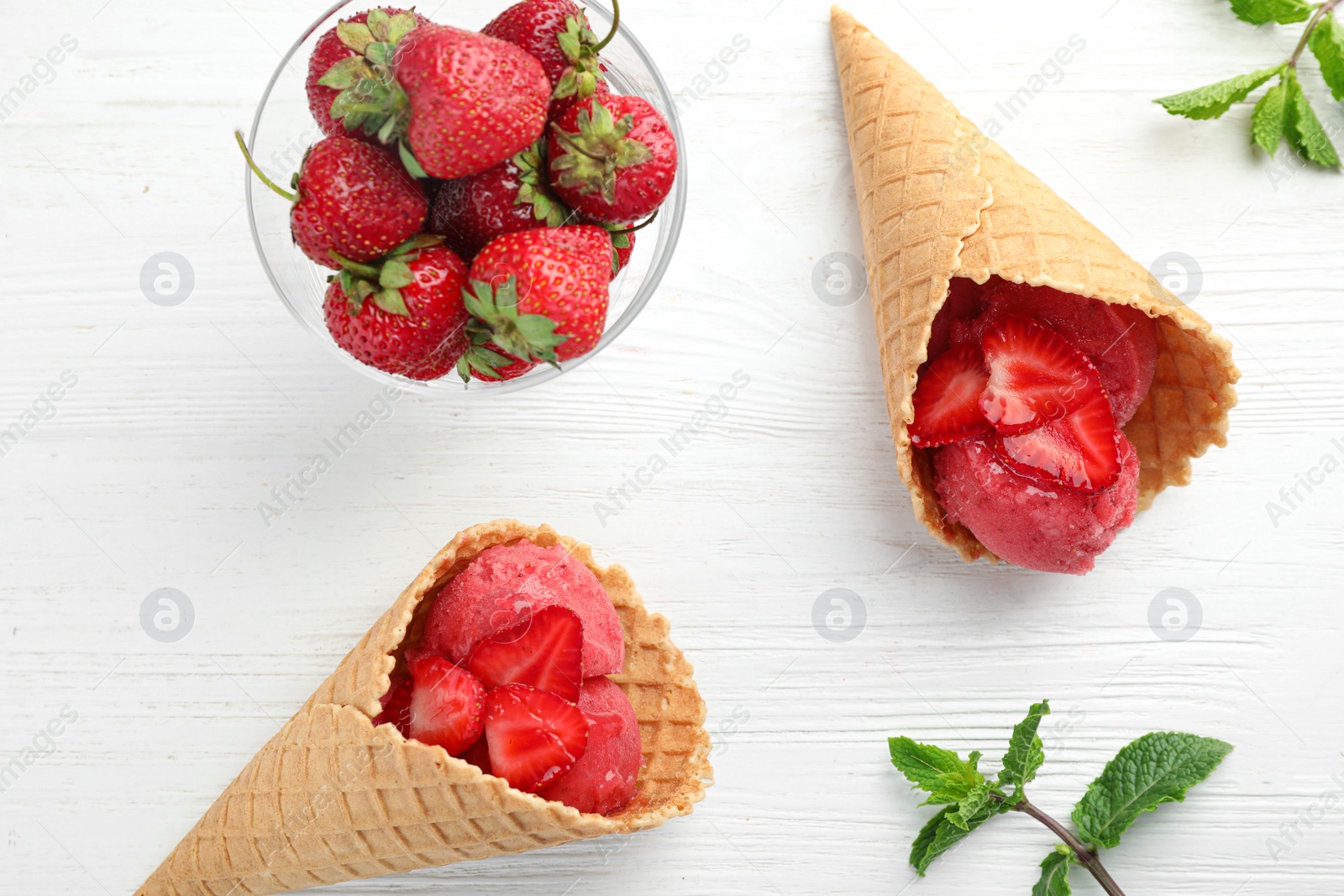 Photo of Delicious strawberry ice cream in wafer cones on white wooden table, flat lay