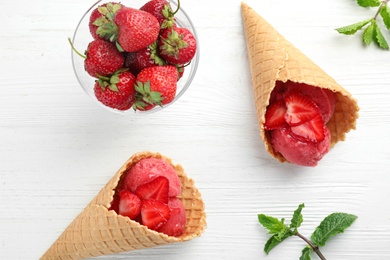 Delicious strawberry ice cream in wafer cones on white wooden table, flat lay