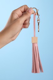 Photo of Woman holding pink leather keychain on light blue background, closeup