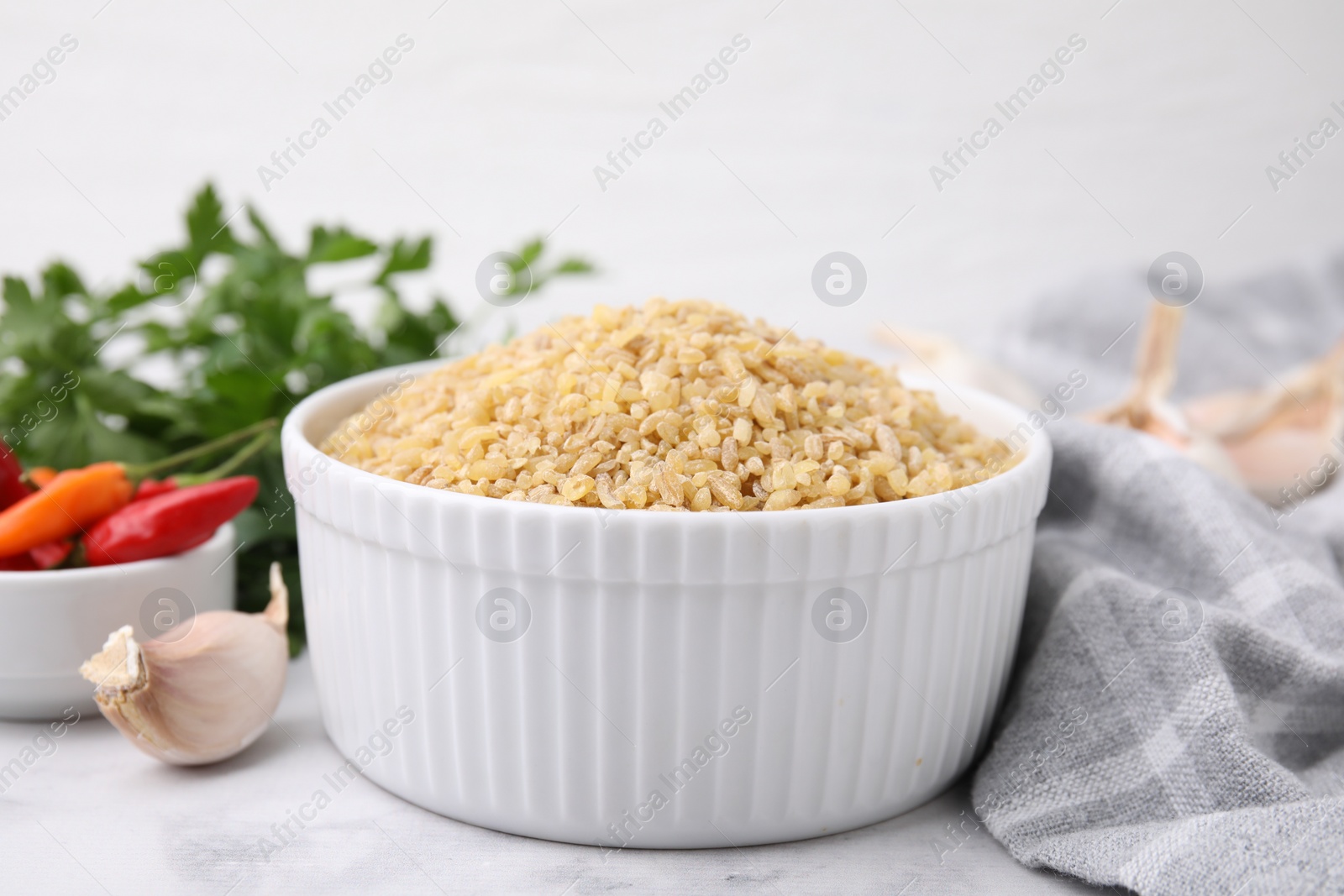 Photo of Raw bulgur in bowl and spices on table, closeup