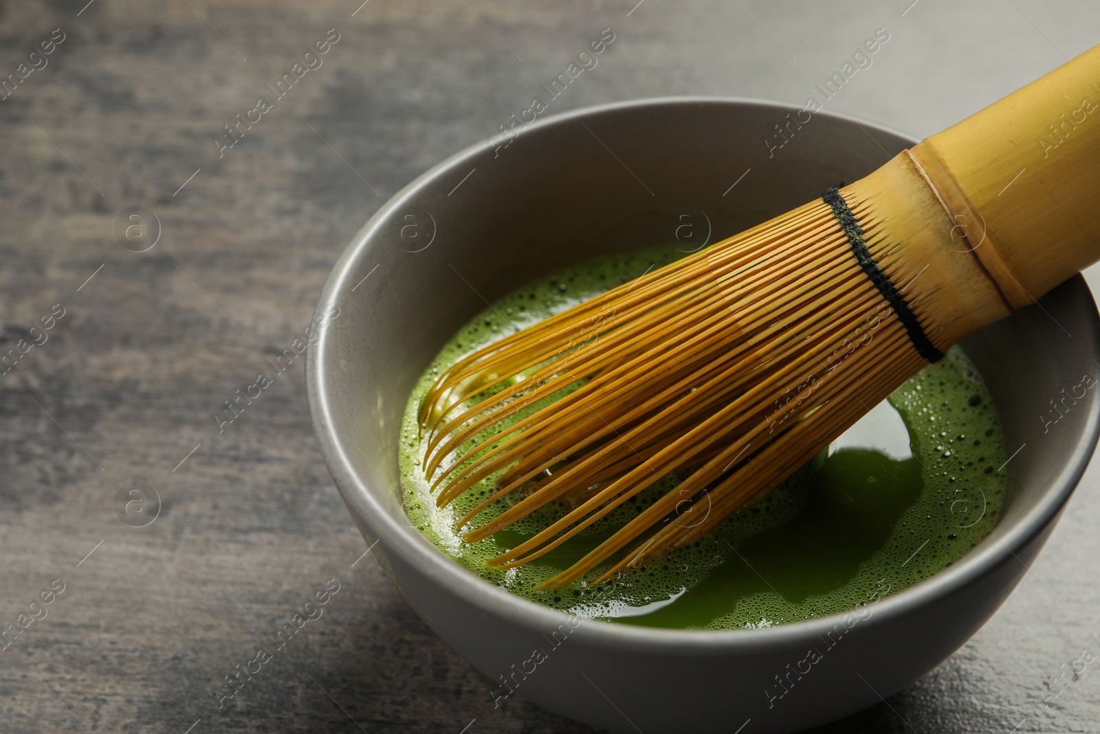 Photo of Cup of fresh matcha tea with bamboo whisk on dark grey table, closeup. Space for text