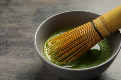Cup of fresh matcha tea with bamboo whisk on dark grey table, closeup. Space for text