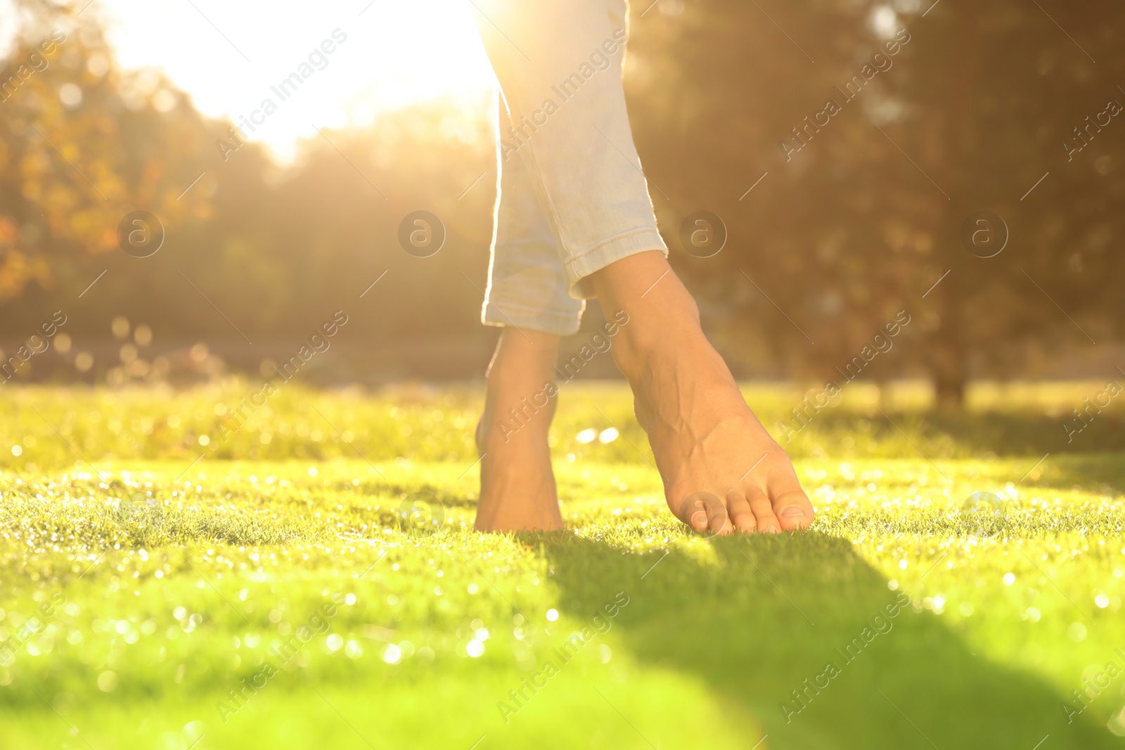 Photo of Young woman walking barefoot on fresh green grass, closeup