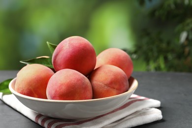 Photo of Fresh peaches and leaves in bowl on grey textured table against blurred green background, closeup