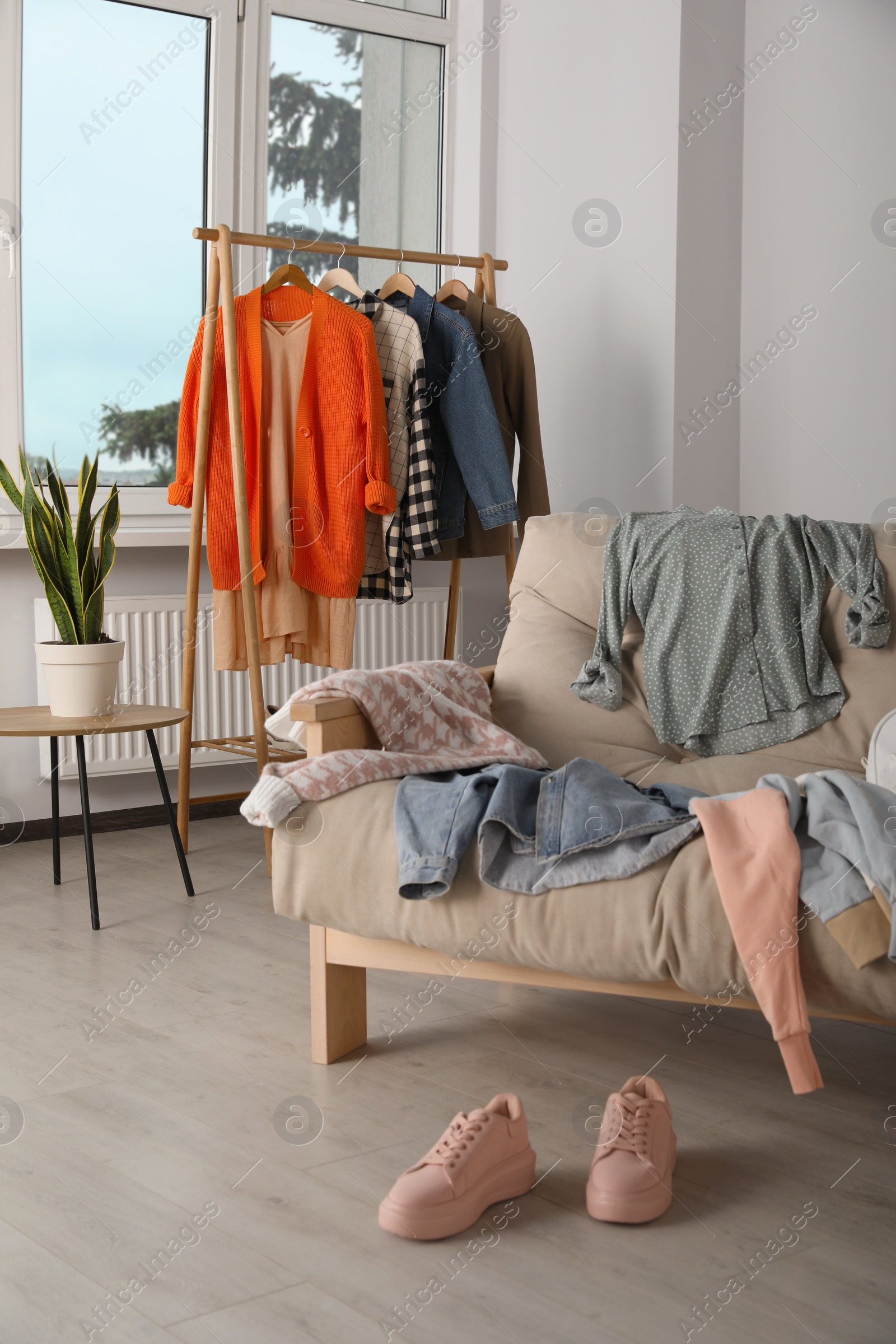 Photo of Messy pile of clothes on sofa and shoes in living room