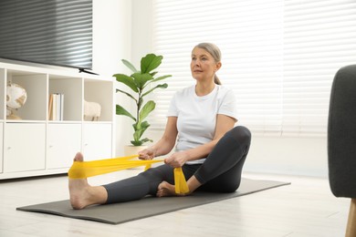 Photo of Senior woman doing exercise with fitness elastic band on mat at home