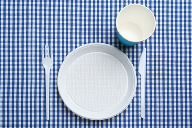 Photo of Table setting with plastic dishware on plaid fabric, flat lay