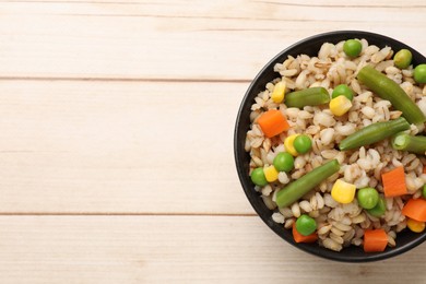 Photo of Delicious pearl barley with vegetables in bowl on wooden table, top view. Space for text