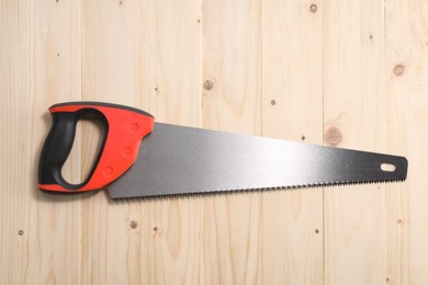 Saw with colorful handle on wooden background, top view