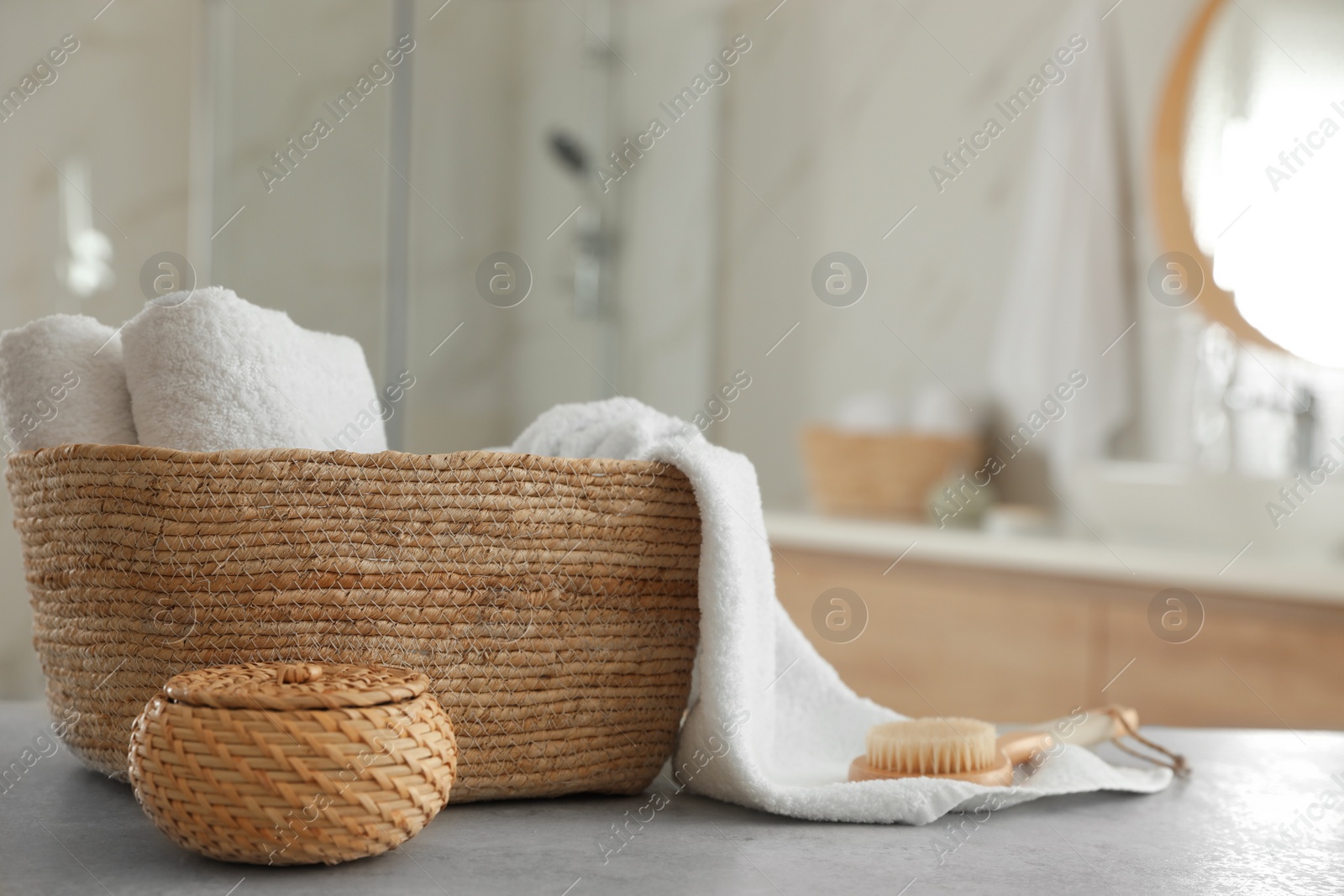 Photo of Wicker basket with clean towels and massage brush on table in bathroom