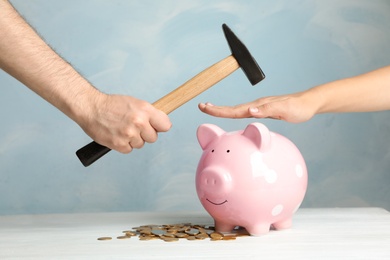 Photo of Woman protecting piggy bank from man with hammer on color background