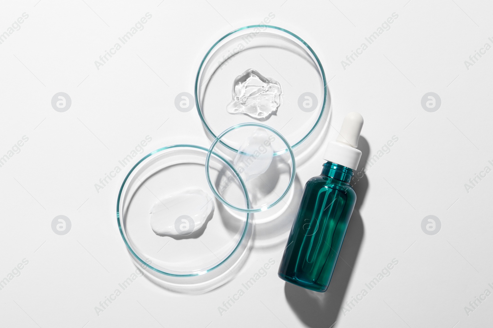 Photo of Bottle of cosmetic serum and petri dishes with samples on white background, flat lay