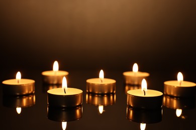 Burning candles on mirror surface in darkness, closeup