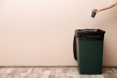 Photo of Young woman throwing coffee cup in trash bin indoors, space for text. Waste recycling