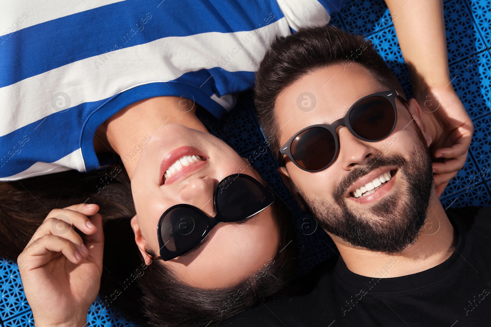 Photo of Beautiful smiling woman and handsome man in sunglasses on blue floor covering outdoors, top view