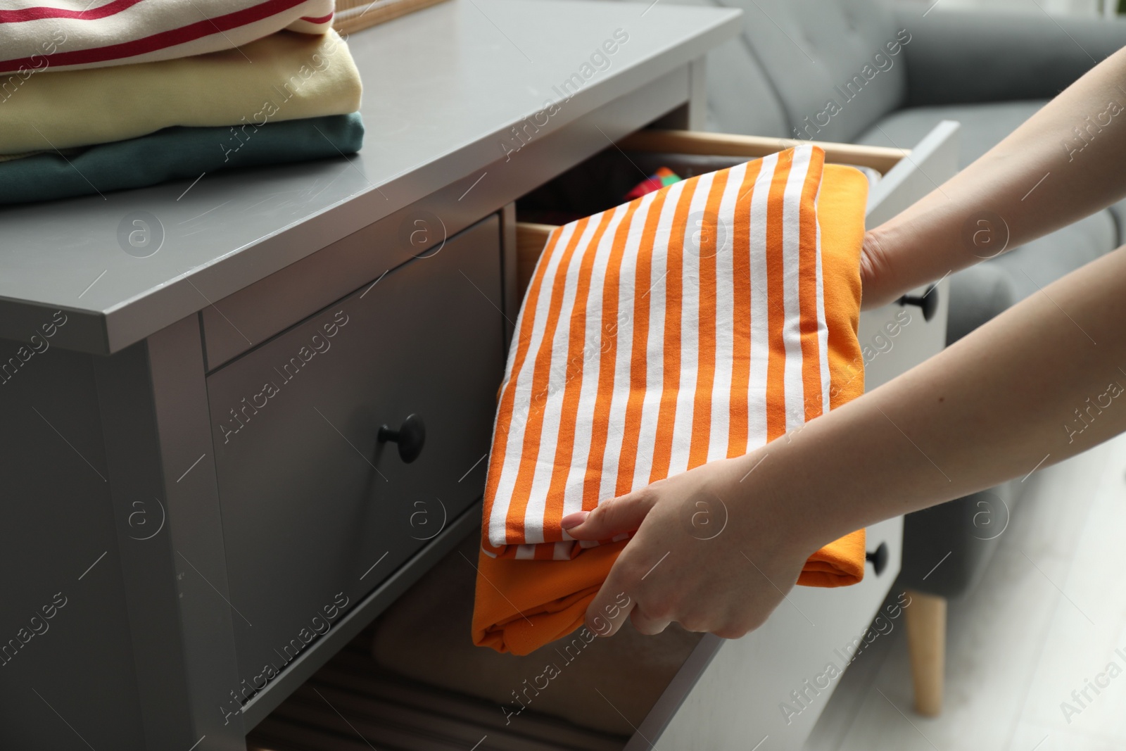 Photo of Woman putting folded clothes into drawer indoors, closeup