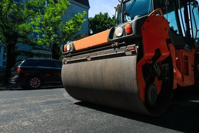 Photo of Roller working on city street, low angle view. Road repairing