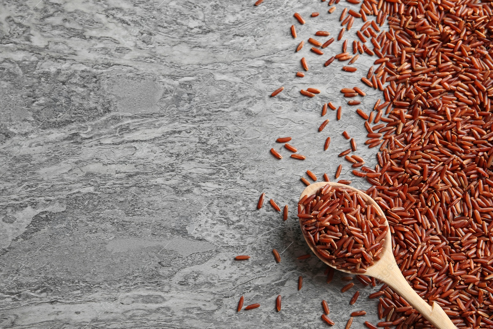 Photo of Brown rice and spoon on grunge background, top view with space for text