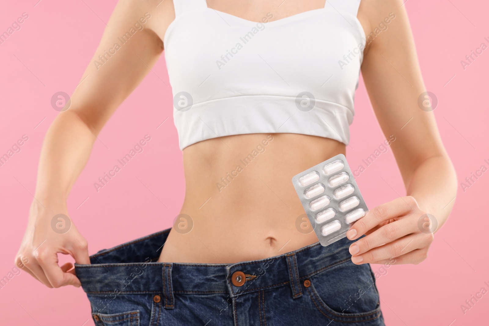 Photo of Slim woman in big jeans with pills on pink background, closeup. Weight loss