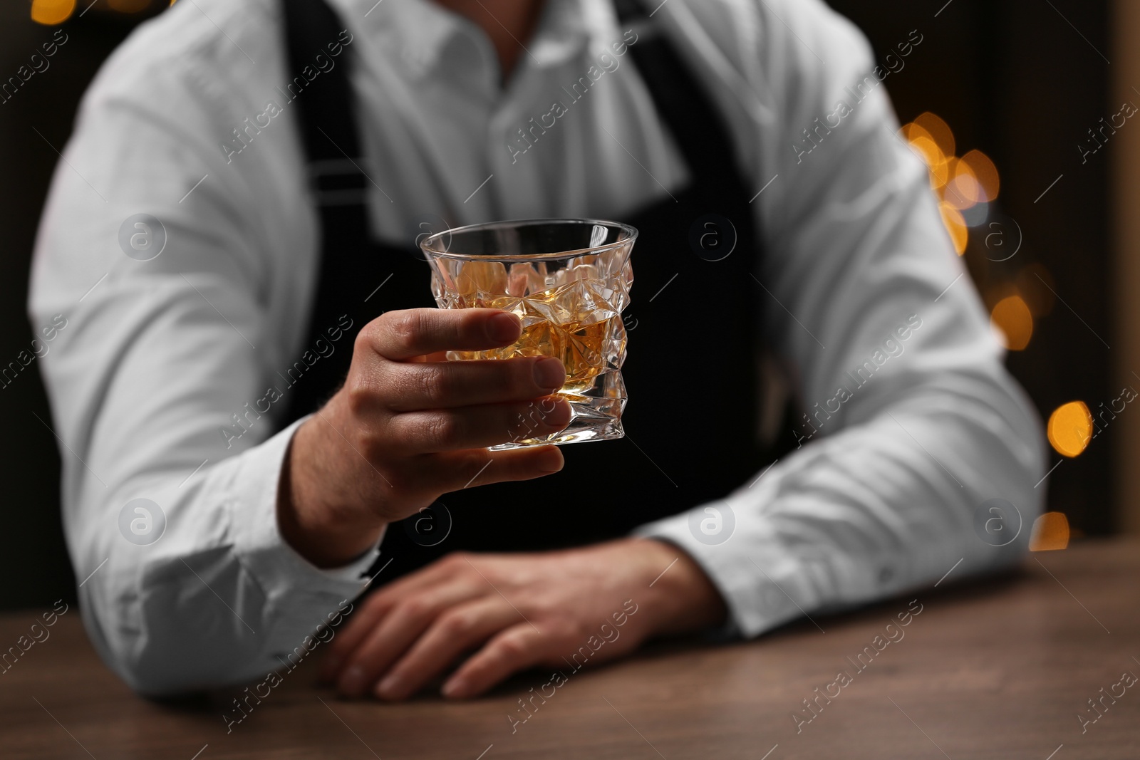 Photo of Bartender with glass of whiskey at bar counter indoors, closeup