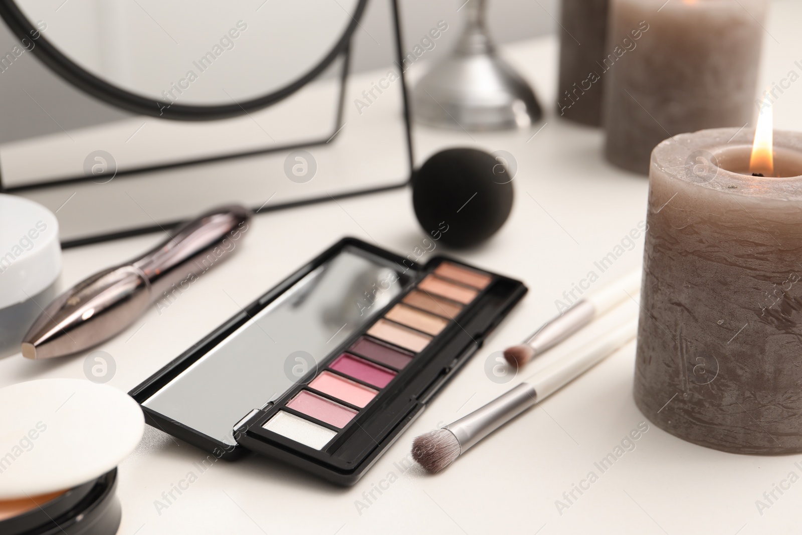 Photo of Mirror, cosmetic products and burning candle on dressing table, closeup