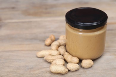 Tasty nut paste in jar and peanuts on wooden table, closeup. Space for text