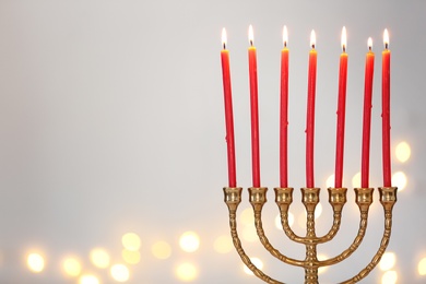 Photo of Golden menorah with burning candles against light grey background and blurred festive lights, space for text