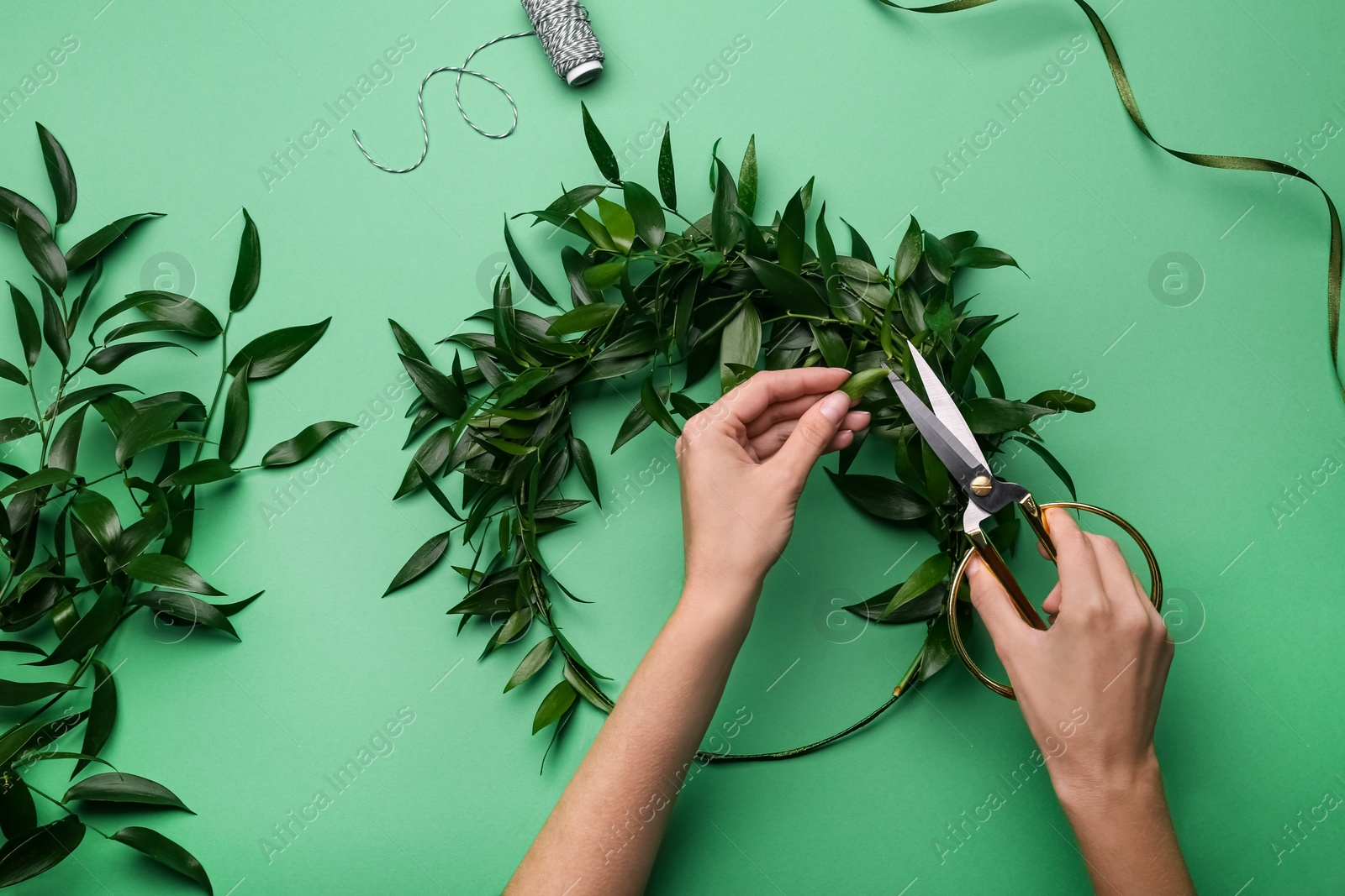 Photo of Florist making beautiful mistletoe wreath on green background, top view. Traditional Christmas decor