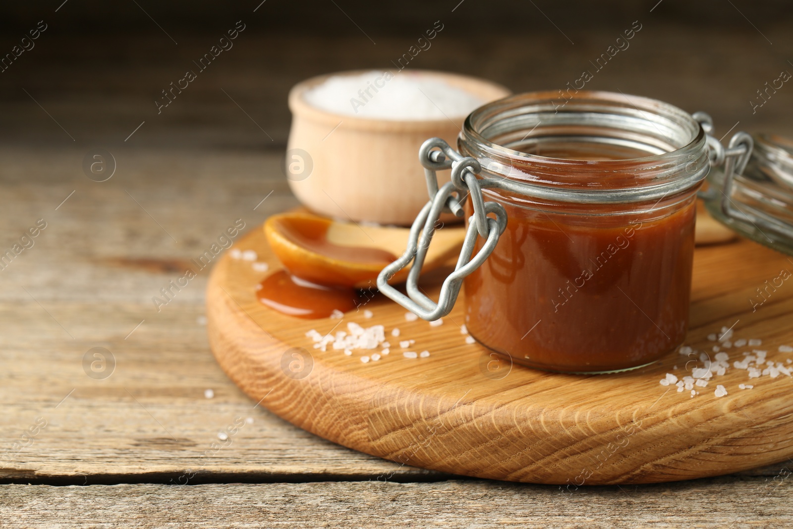 Photo of Tasty salted caramel in jar and salt on wooden table, closeup. Space for text