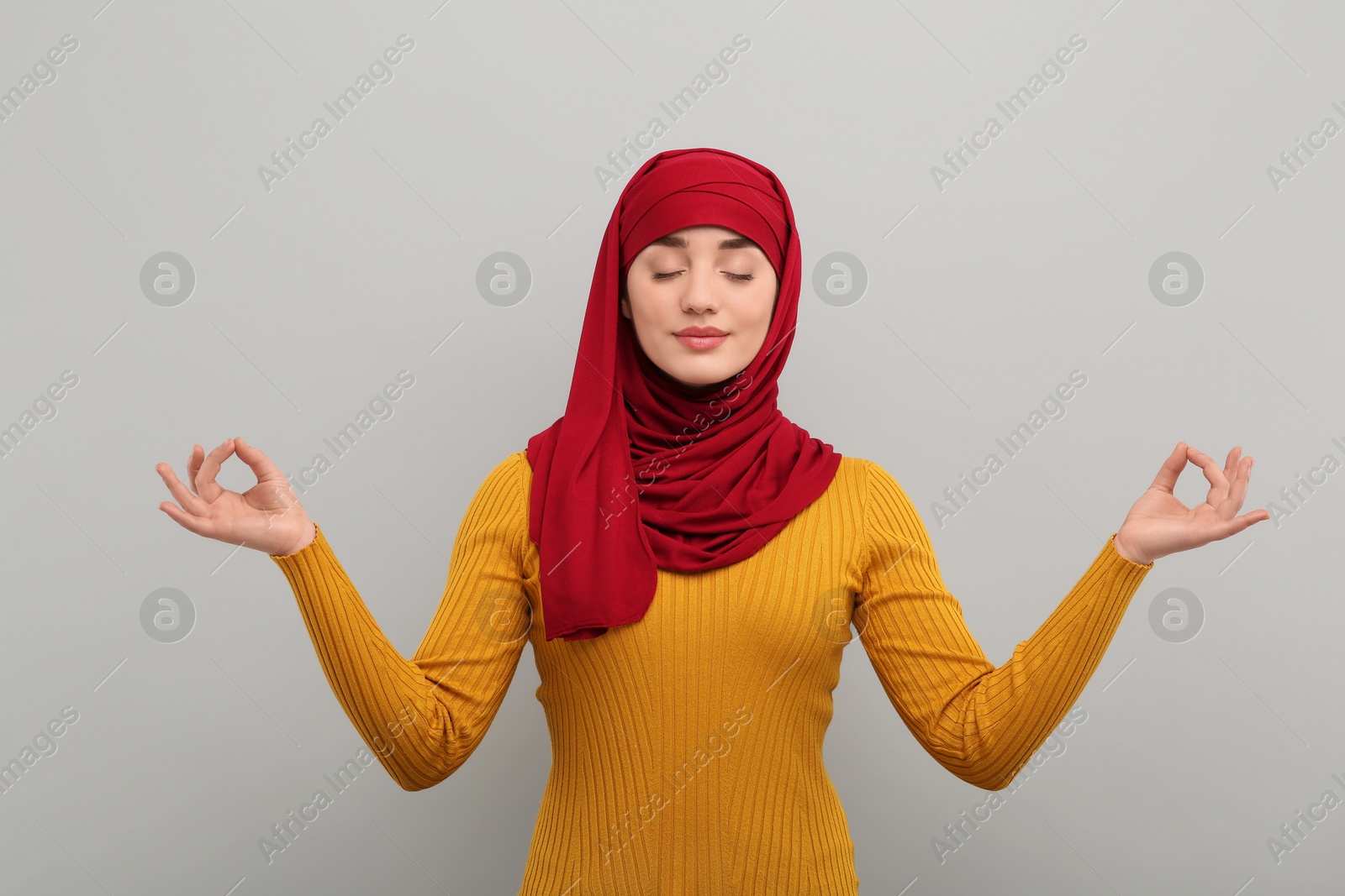 Photo of Muslim woman in hijab meditating on light gray background