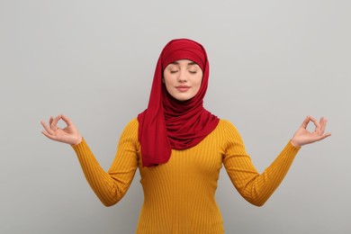 Muslim woman in hijab meditating on light gray background