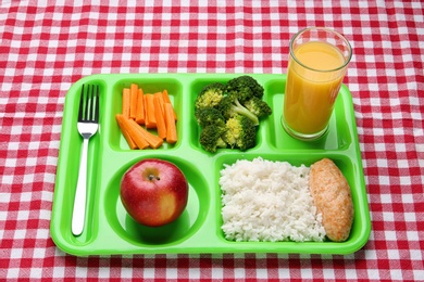 Serving tray with healthy food on checkered background. School lunch