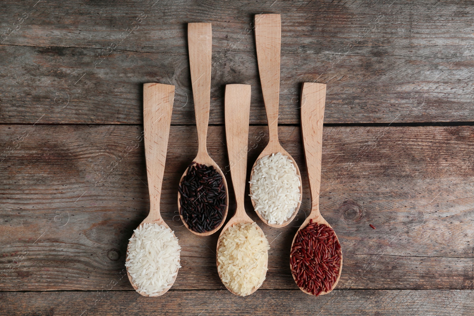 Photo of Flat lay composition with brown and other types of rice in spoons on wooden background